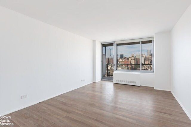 270 W 17th St Unit 14B, New York City, NY 10011 - spare room with radiator heating unit, wood finished floors, and baseboards
