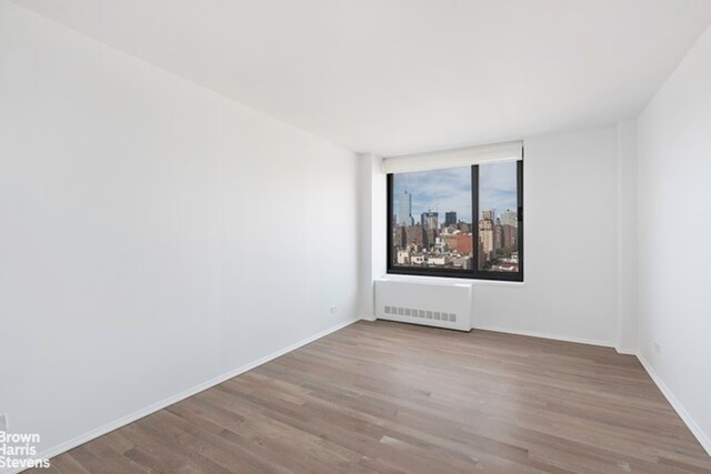 270 W 17th St Unit 14B, New York City, NY 10011 - spare room featuring radiator heating unit, wood finished floors, and baseboards
