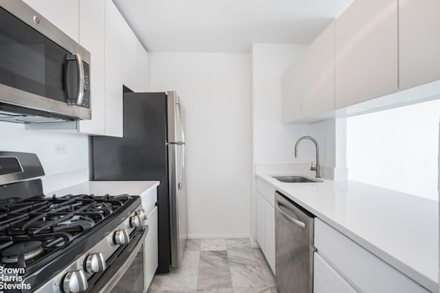 kitchen with appliances with stainless steel finishes, a sink, light countertops, white cabinetry, and light marble finish floors