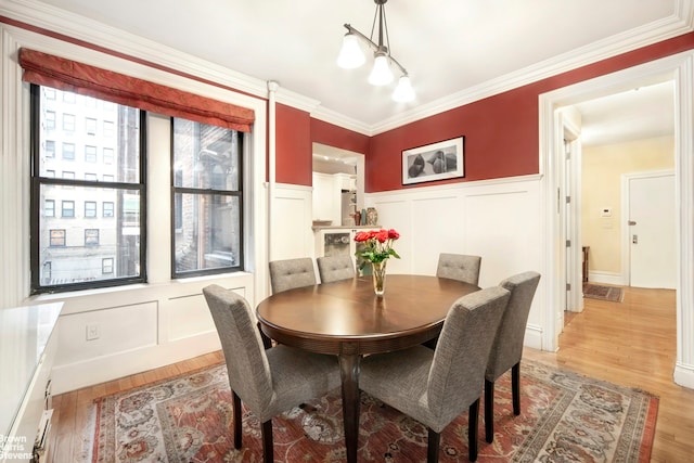 dining area with a decorative wall, light wood-style floors, and ornamental molding