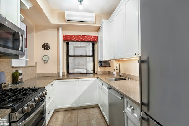 kitchen with light stone countertops, a wall mounted AC, a sink, stainless steel appliances, and white cabinets