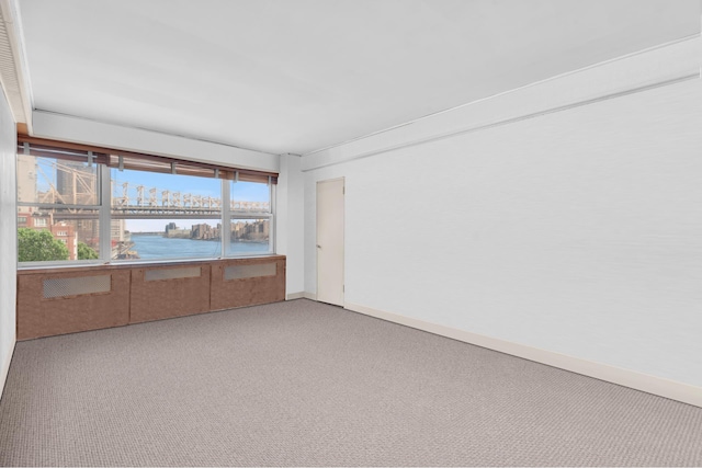 empty room featuring a water view, baseboards, and carpet floors