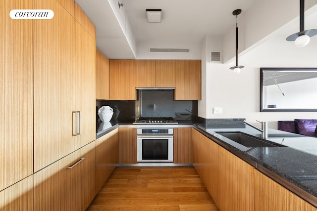 kitchen featuring oven, stainless steel gas stovetop, dark stone counters, decorative backsplash, and light wood-style floors