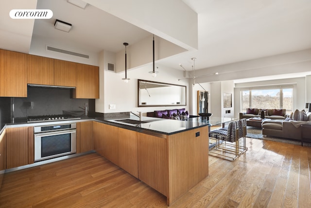 kitchen featuring stainless steel oven, a sink, open floor plan, and light wood-type flooring