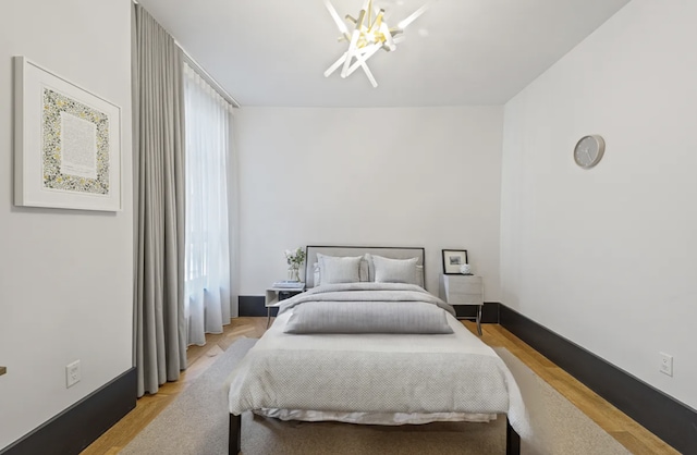 bedroom featuring baseboards, light wood-style floors, and an inviting chandelier