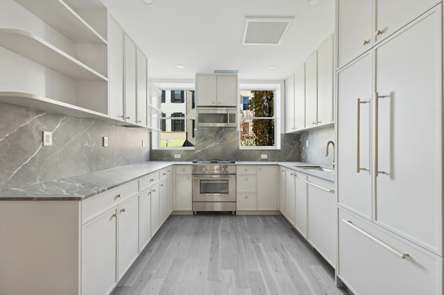 kitchen with light wood finished floors, tasteful backsplash, a sink, high end appliances, and open shelves