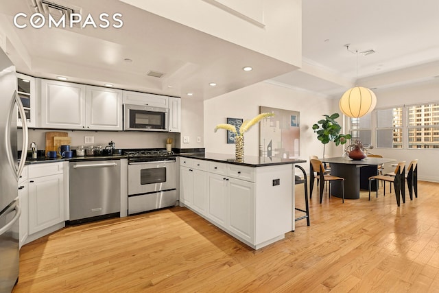 kitchen with dark countertops, a tray ceiling, appliances with stainless steel finishes, a peninsula, and light wood-style floors