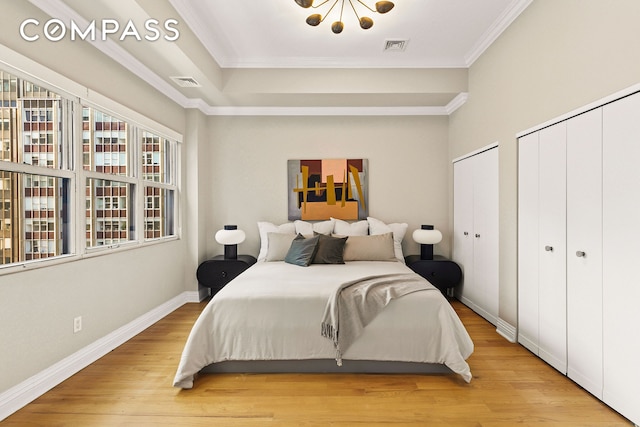 bedroom with light wood finished floors, visible vents, two closets, crown molding, and baseboards