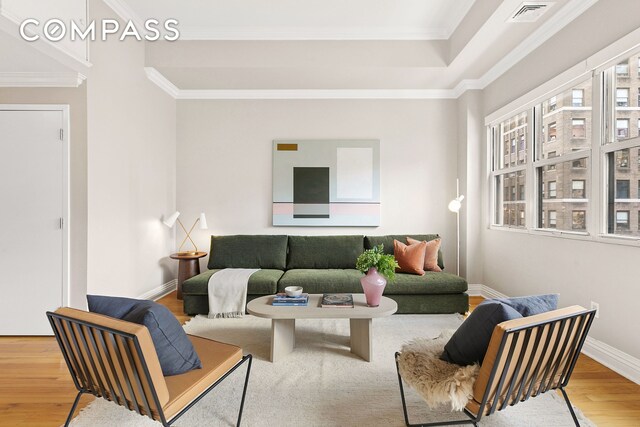 living room with crown molding, wood finished floors, visible vents, and baseboards