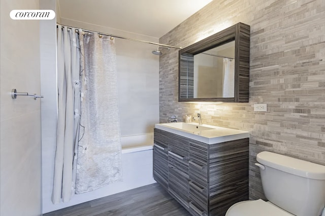 full bath featuring shower / bath combo with shower curtain, toilet, vanity, wood finished floors, and tile walls