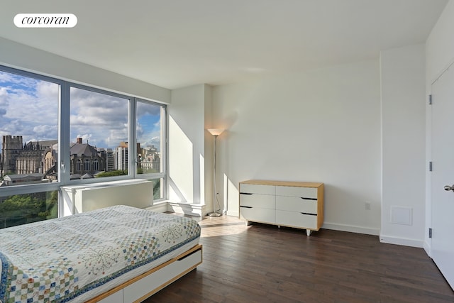 bedroom with dark wood finished floors, visible vents, a city view, and baseboards