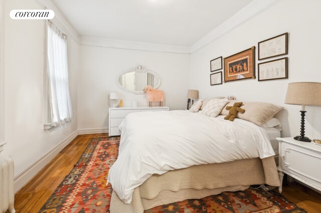 bedroom with visible vents, radiator heating unit, crown molding, light wood finished floors, and baseboards