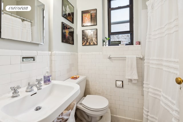 bathroom with a sink, a wainscoted wall, toilet, and tile walls