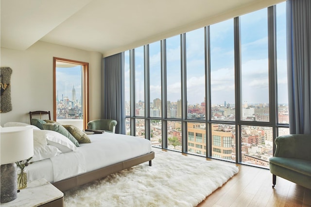 bedroom with multiple windows, a city view, wood finished floors, and floor to ceiling windows