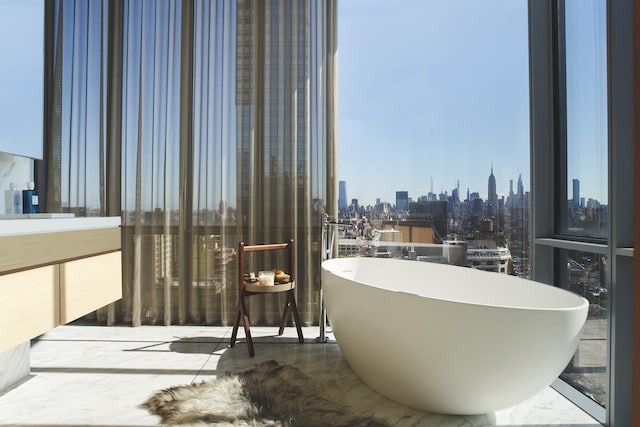 full bathroom with a city view, a soaking tub, vanity, and a wall of windows