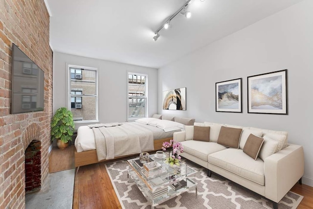 bedroom featuring a fireplace, brick wall, rail lighting, and wood finished floors