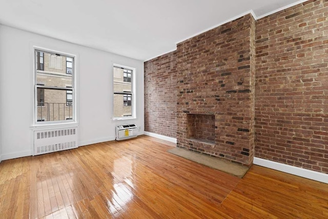 unfurnished living room featuring brick wall, radiator heating unit, baseboards, and wood-type flooring