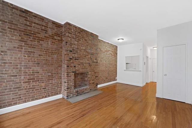 unfurnished living room featuring a brick fireplace, brick wall, baseboards, and hardwood / wood-style flooring