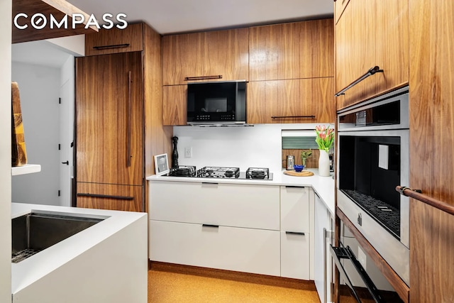 kitchen with light countertops, brown cabinetry, black appliances, modern cabinets, and a sink