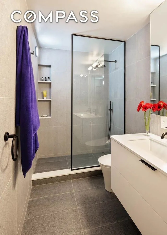 bathroom featuring toilet, tile walls, vanity, and walk in shower