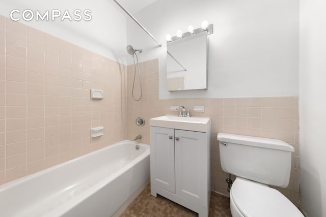 bathroom with vanity, wainscoting, toilet, tile walls, and  shower combination
