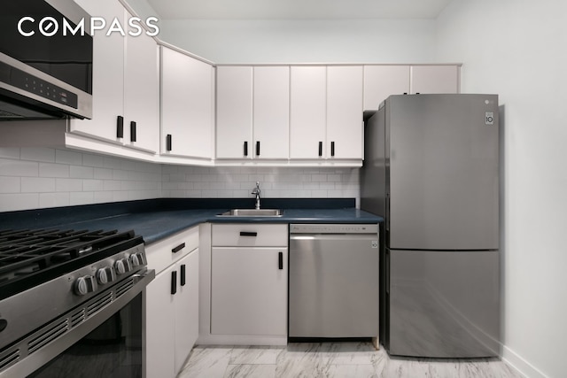 kitchen featuring white cabinets, stainless steel appliances, dark countertops, and a sink