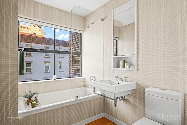 bathroom with wood finished floors, a sink, a relaxing tiled tub, tile walls, and toilet