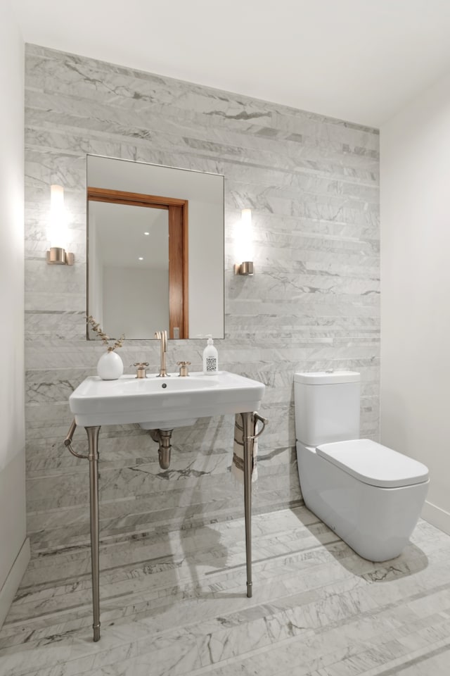 half bathroom with marble finish floor, toilet, and tile walls