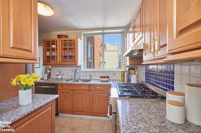 kitchen featuring stainless steel gas stove, a sink, under cabinet range hood, brown cabinetry, and decorative backsplash