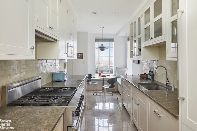 kitchen with dark stone countertops, white cabinets, stainless steel stove, and a sink