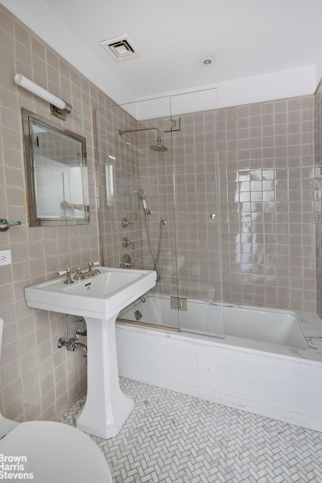 bathroom with tile patterned flooring, visible vents, toilet, combined bath / shower with glass door, and tile walls