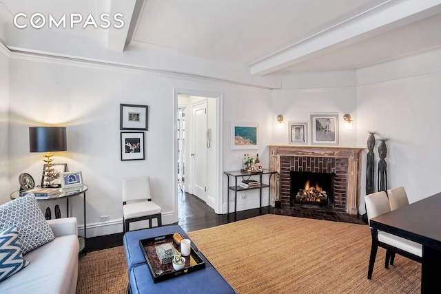 living room with beamed ceiling, baseboards, a brick fireplace, and wood finished floors