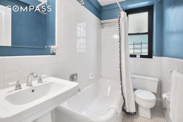 full bath featuring tile patterned floors, shower / bath combo with shower curtain, toilet, a sink, and tile walls