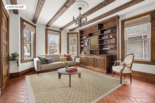 living room featuring baseboards, beamed ceiling, built in features, brick floor, and a notable chandelier