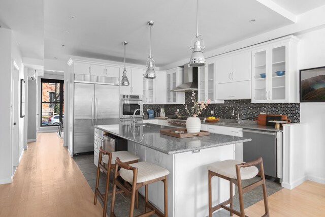 kitchen with a center island with sink, a kitchen bar, decorative backsplash, stainless steel appliances, and wall chimney exhaust hood