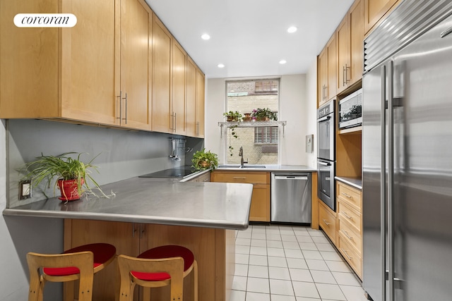 kitchen featuring appliances with stainless steel finishes, light tile patterned floors, a sink, a kitchen breakfast bar, and a peninsula