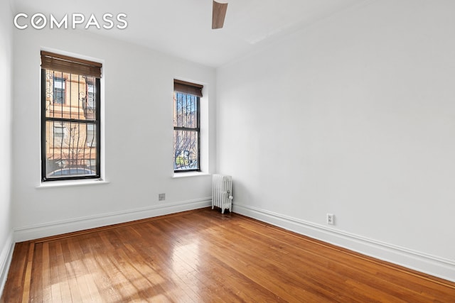 empty room with radiator, baseboards, a ceiling fan, and hardwood / wood-style floors