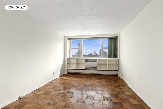 empty room featuring baseboards, visible vents, a baseboard radiator, a textured ceiling, and a city view