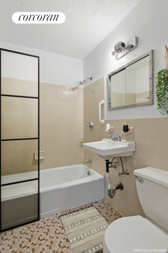 full bathroom with tile walls, toilet, shower / tub combination, a textured ceiling, and a sink