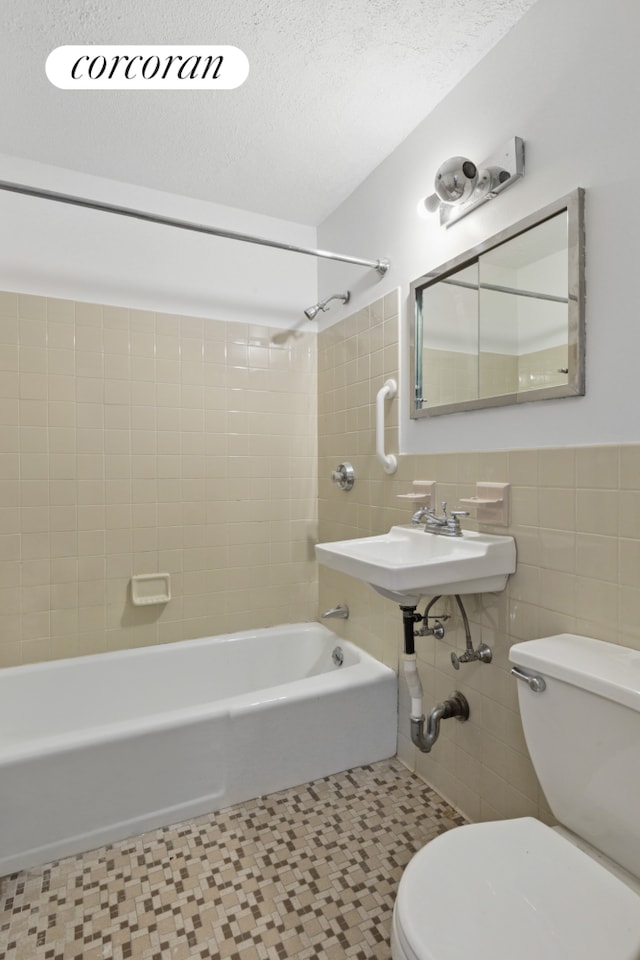 full bath featuring  shower combination, a sink, a textured ceiling, tile walls, and toilet