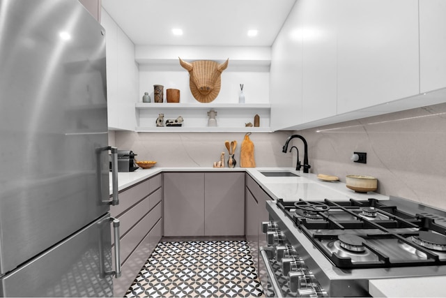 kitchen featuring backsplash, open shelves, gray cabinets, freestanding refrigerator, and a sink