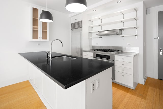 kitchen featuring open shelves, stainless steel appliances, a sink, white cabinetry, and wall chimney exhaust hood