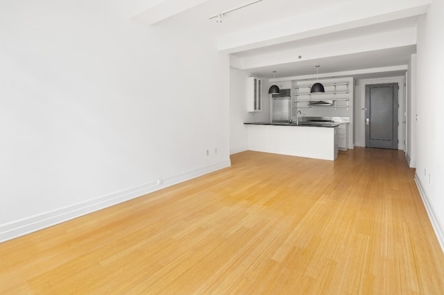 unfurnished living room featuring a sink, baseboards, light wood-style floors, and track lighting