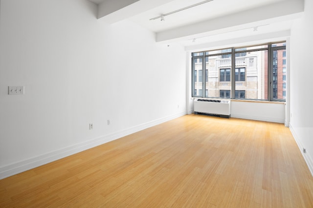 unfurnished room with track lighting, baseboards, radiator heating unit, and light wood-style floors