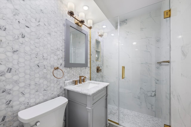 full bath featuring a marble finish shower, toilet, and vanity