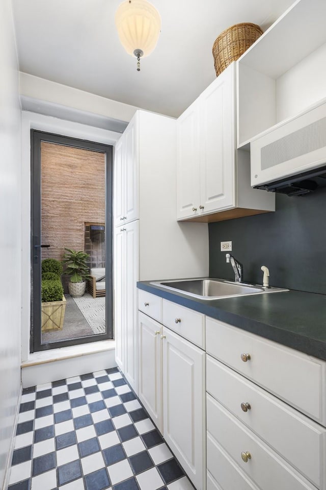 kitchen with tile patterned floors, white cabinets, dark countertops, and a sink