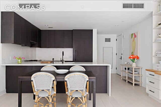kitchen with light countertops, a sink, gas cooktop, a kitchen breakfast bar, and light wood-style flooring