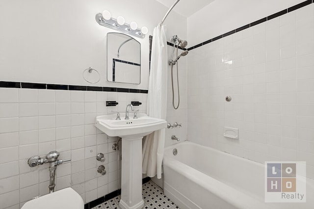 full bath featuring a wainscoted wall, shower / bath combo with shower curtain, toilet, a sink, and tile walls