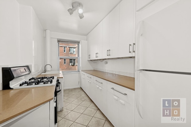 kitchen with a sink, white cabinetry, gas stove, freestanding refrigerator, and light tile patterned floors