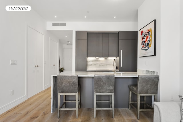 kitchen with modern cabinets, a kitchen breakfast bar, light countertops, light wood finished floors, and gray cabinetry